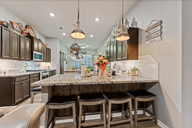 9791 Waller St, Conroe, TX 77303 - kitchen with tasteful backsplash, dark brown cabinetry, white microwave, a peninsula, and light stone countertops