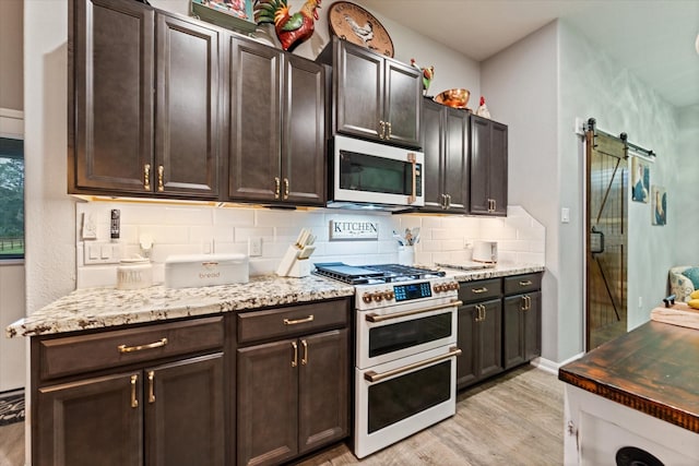 9791 Waller St, Conroe, TX 77303 - kitchen with white microwave, tasteful backsplash, a barn door, light stone counters, and range with two ovens