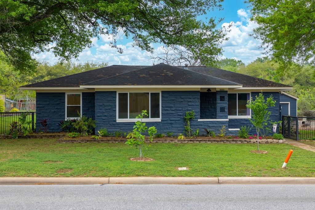 ranch-style home with stone siding, fence, and a front lawn