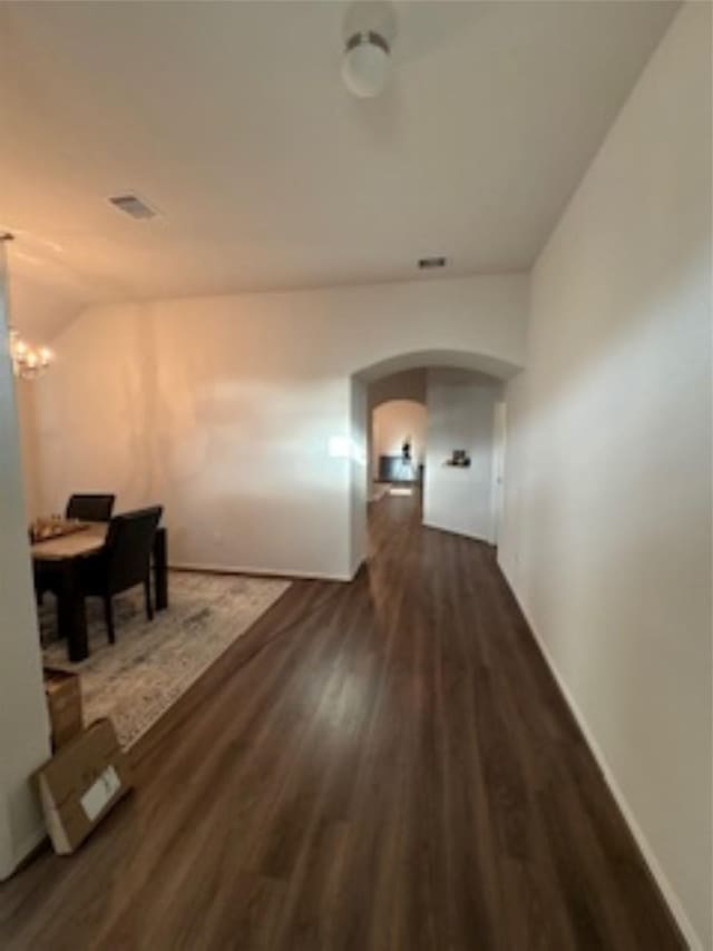 hallway with lofted ceiling, an inviting chandelier, dark wood-style flooring, baseboards, and arched walkways