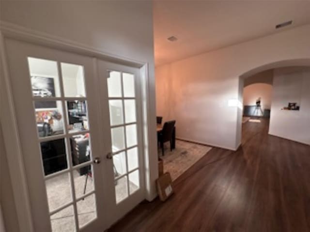 hallway featuring arched walkways, wood finished floors, and french doors