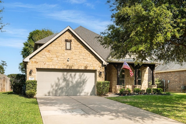 view of front facade featuring driveway, a front yard, stone siding, roof with shingles, and a garage