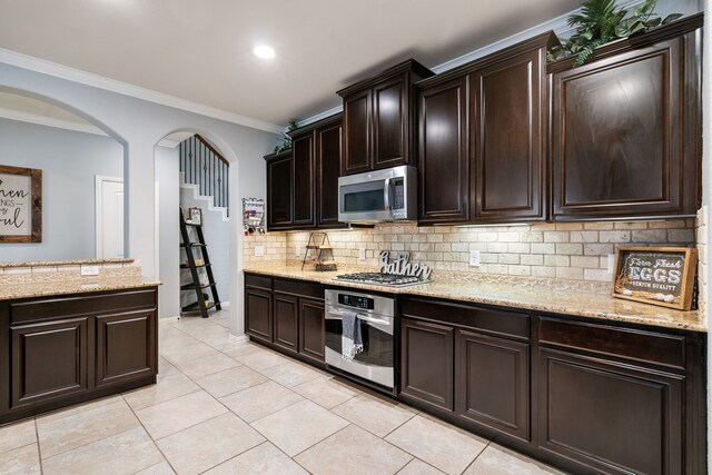kitchen with ornamental molding, stainless steel appliances, decorative backsplash, arched walkways, and light stone counters