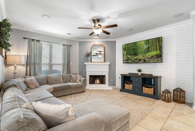 living area featuring crown molding, light tile patterned floors, visible vents, a warm lit fireplace, and ceiling fan