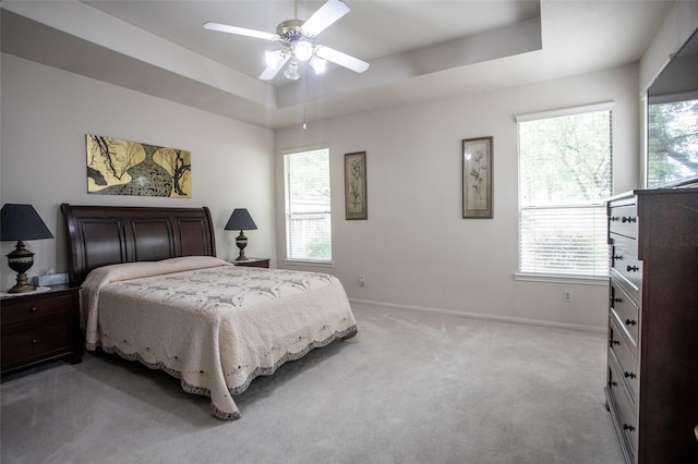bedroom featuring a tray ceiling, light colored carpet, baseboards, and ceiling fan