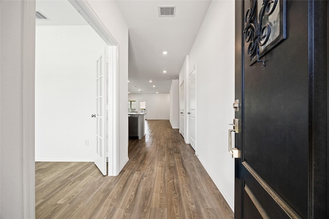 hall featuring baseboards, wood finished floors, visible vents, and recessed lighting