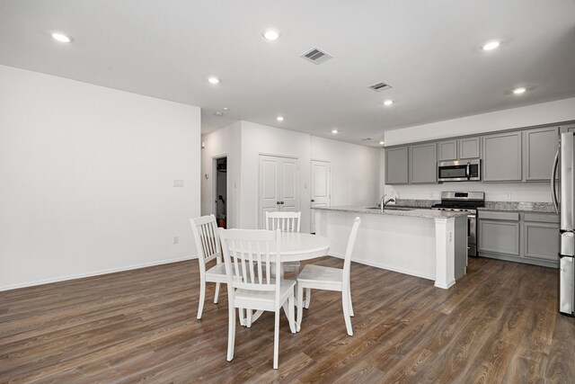 kitchen with dark wood finished floors, an island with sink, appliances with stainless steel finishes, and gray cabinets