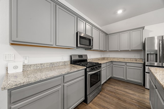 kitchen with light stone counters, appliances with stainless steel finishes, gray cabinets, and dark wood-style flooring