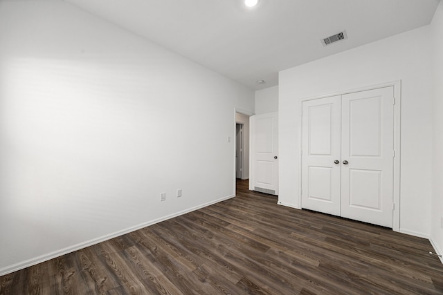 unfurnished bedroom featuring a closet, dark wood finished floors, visible vents, and baseboards