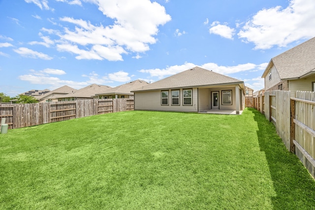 rear view of property featuring a yard, a patio area, a shingled roof, and a fenced backyard