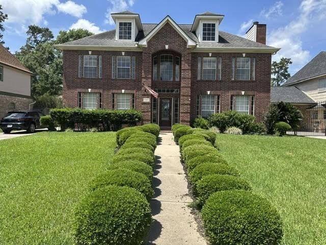colonial home featuring a front lawn, a chimney, and brick siding