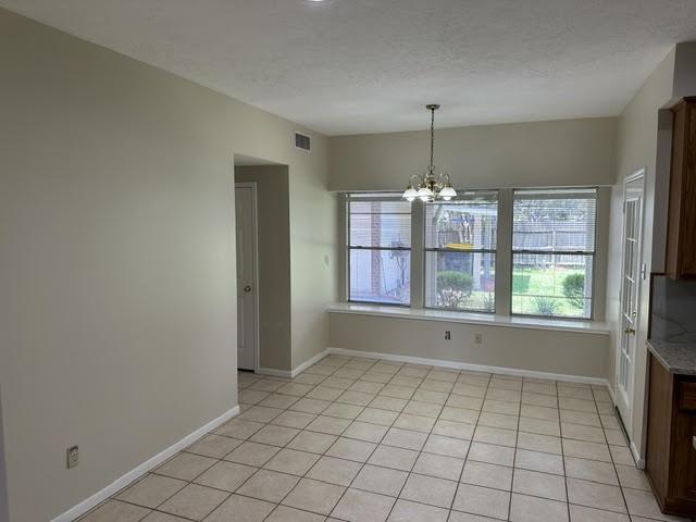 unfurnished dining area with light tile patterned floors, visible vents, plenty of natural light, and a notable chandelier