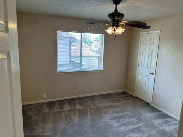 carpeted spare room featuring a ceiling fan and baseboards