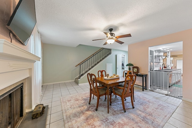 6506 Kentwick Dr, Houston, TX 77084 - tiled dining space featuring a textured ceiling, stairs, ceiling fan, and a fireplace
