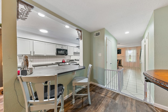 6506 Kentwick Dr, Houston, TX 77084 - kitchen with black microwave, tasteful backsplash, dark wood-style floors, stove, and visible vents
