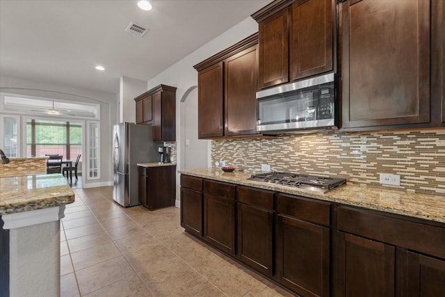kitchen featuring tasteful backsplash, light stone counters, dark brown cabinets, visible vents, and appliances with stainless steel finishes