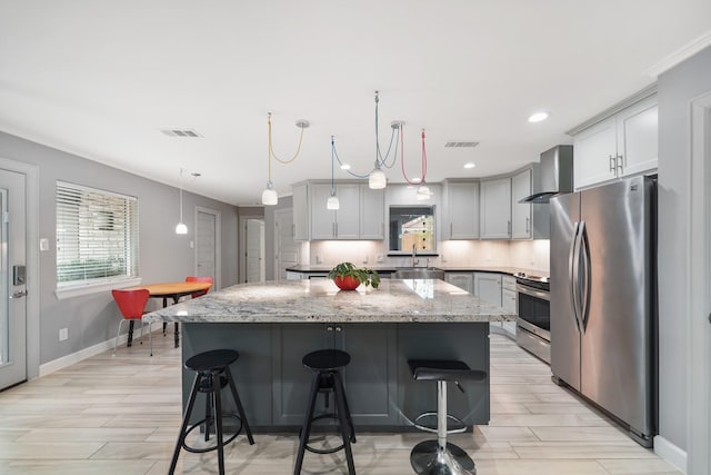 kitchen with appliances with stainless steel finishes, wall chimney exhaust hood, visible vents, and a kitchen island