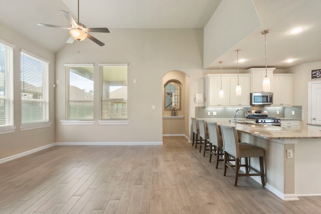 16875 Olympic National Dr, Humble, TX 77346 - kitchen featuring appliances with stainless steel finishes, light wood-style floors, a kitchen bar, a ceiling fan, and lofted ceiling