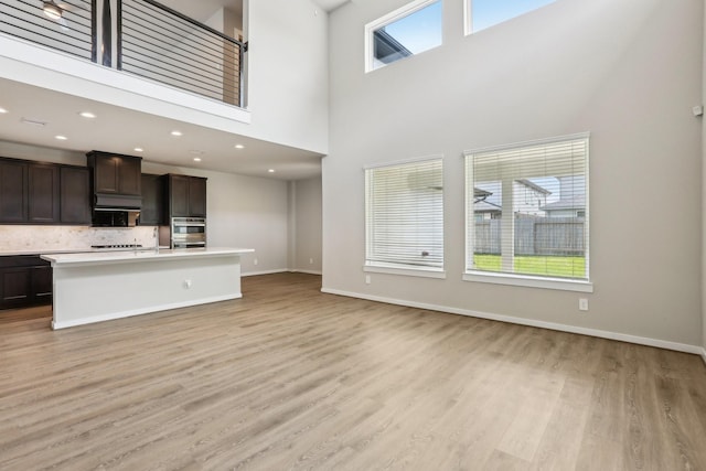 unfurnished living room with light wood-style floors, a towering ceiling, baseboards, and recessed lighting
