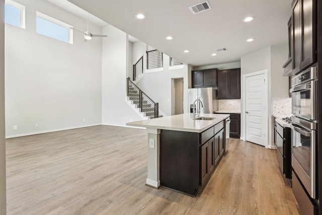 kitchen featuring ceiling fan, backsplash, light countertops, dark brown cabinetry, and light wood finished floors