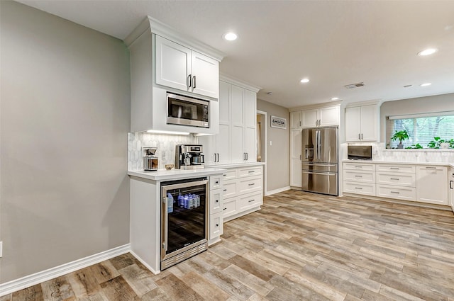 22814 Wren Ln, Tomball, TX 77377 - kitchen with stainless steel appliances, wine cooler, tasteful backsplash, light wood-style floors, and white cabinetry