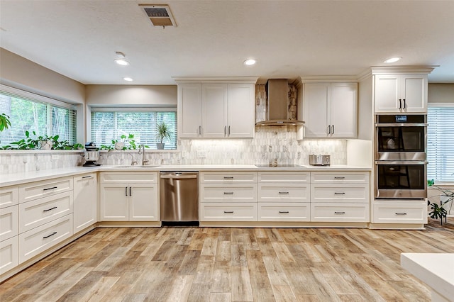 22814 Wren Ln, Tomball, TX 77377 - kitchen featuring wall chimney exhaust hood, appliances with stainless steel finishes, a sink, light wood finished floors, and white cabinets