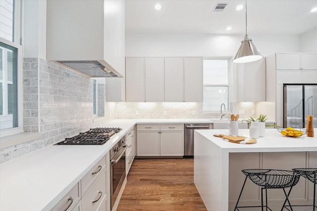 kitchen with decorative backsplash, a breakfast bar, custom range hood, appliances with stainless steel finishes, and visible vents