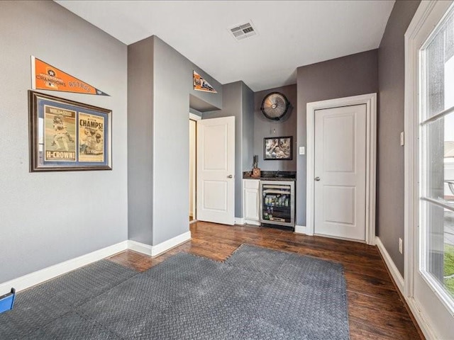 interior space with wine cooler, visible vents, baseboards, and dark wood-style floors