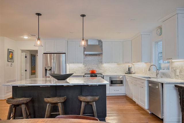2311 Branard St, Houston, TX 77098 - kitchen with light wood finished floors, a kitchen breakfast bar, stainless steel appliances, wall chimney range hood, and a sink
