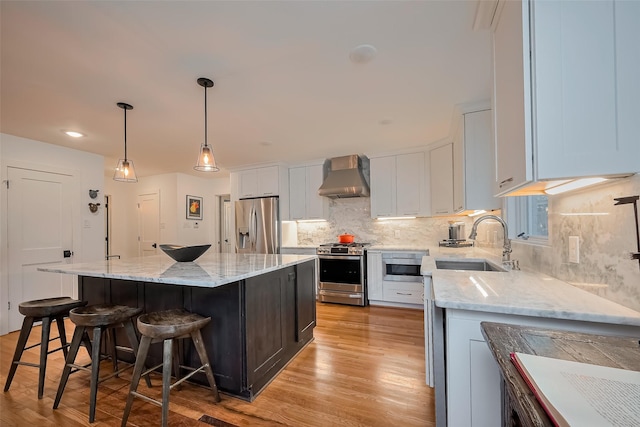 2311 Branard St, Houston, TX 77098 - kitchen with light wood finished floors, stainless steel appliances, wall chimney range hood, a sink, and a center island