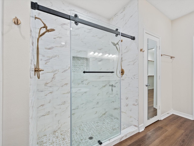 bathroom with a marble finish shower, wood finished floors, and baseboards