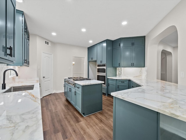 kitchen with a sink, light stone countertops, arched walkways, dark wood finished floors, and recessed lighting