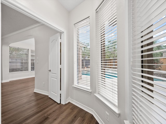 corridor with dark wood-style flooring, baseboards, healthy amount of natural light, and arched walkways