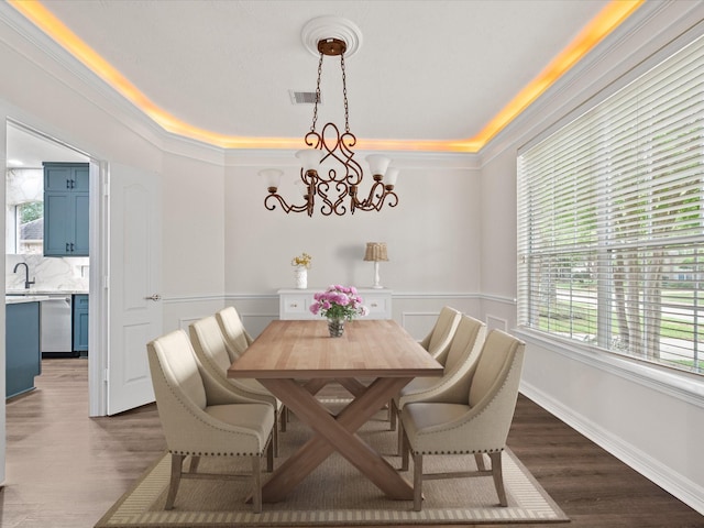 dining area with a chandelier, a wainscoted wall, dark wood-type flooring, ornamental molding, and a raised ceiling