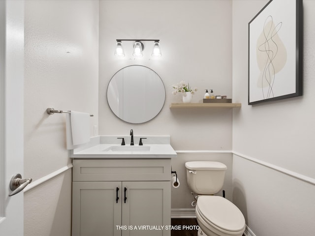 half bathroom with vanity, toilet, and baseboards