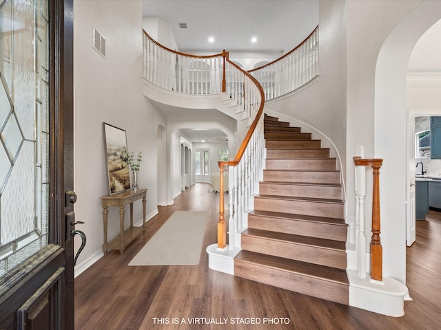 foyer entrance with arched walkways, wood finished floors, a towering ceiling, baseboards, and stairs