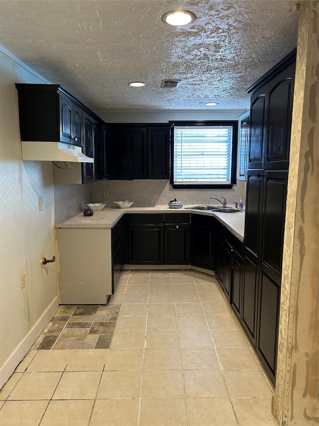 kitchen featuring a sink, light countertops, baseboards, dark cabinetry, and light tile patterned floors