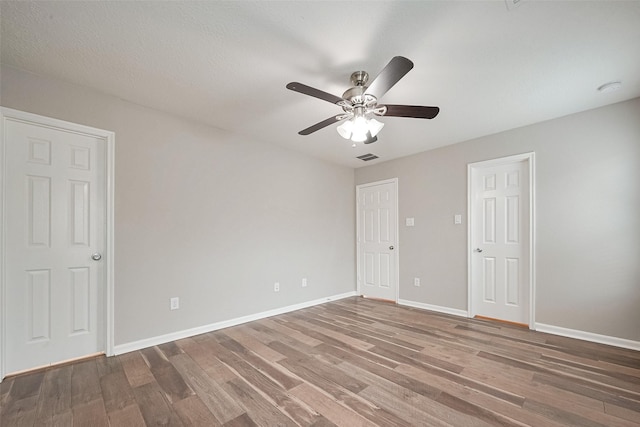 empty room with a ceiling fan, visible vents, baseboards, and wood finished floors