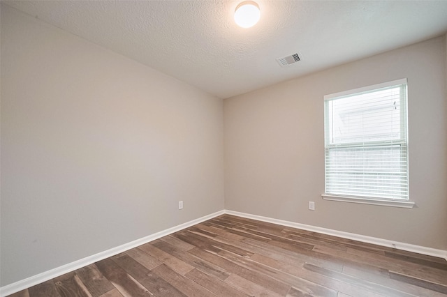 unfurnished room with dark wood-style floors, visible vents, baseboards, and a textured ceiling