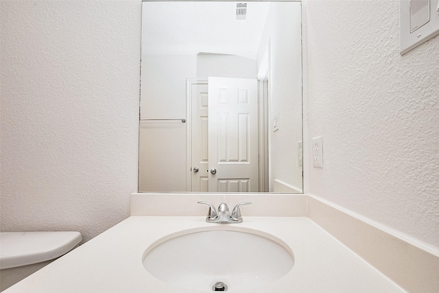 bathroom with visible vents, a textured wall, toilet, and vanity