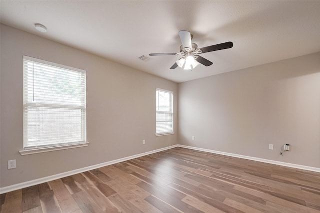 spare room with baseboards, visible vents, wood finished floors, and a ceiling fan