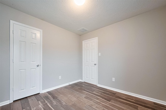 empty room featuring dark wood-style floors, visible vents, baseboards, and a textured ceiling