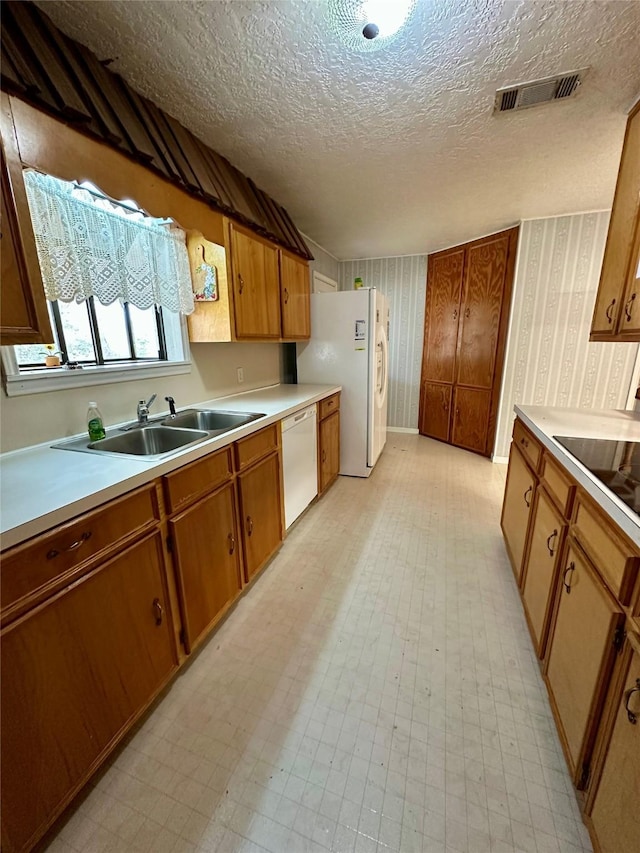 kitchen with light floors, wallpapered walls, white appliances, and a sink