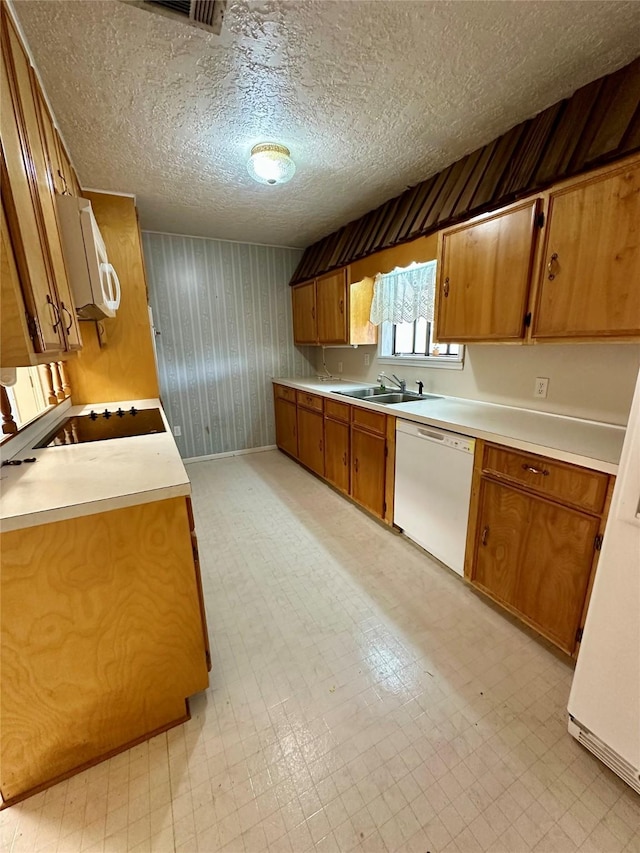 kitchen featuring a textured ceiling, a sink, white appliances, brown cabinets, and light countertops
