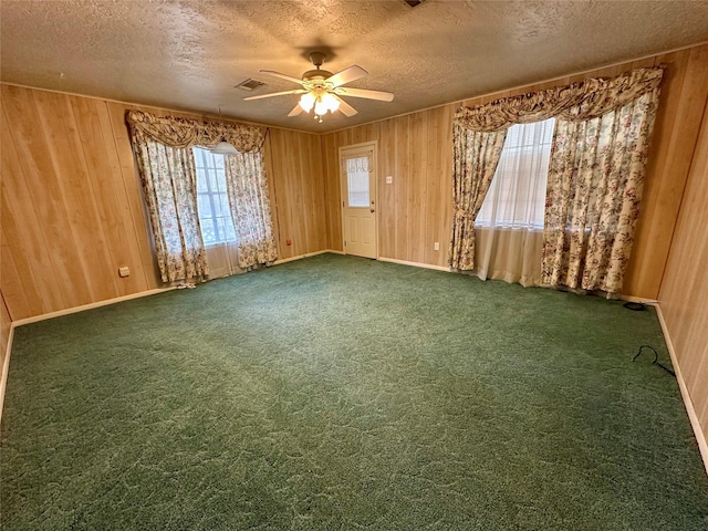 spare room featuring a textured ceiling, wood walls, baseboards, and a ceiling fan