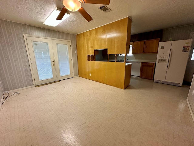 kitchen with brown cabinets, wallpapered walls, visible vents, a ceiling fan, and white appliances