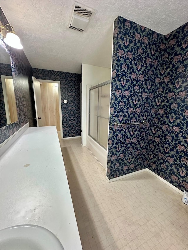 full bath featuring visible vents, a shower with door, a textured ceiling, and wallpapered walls