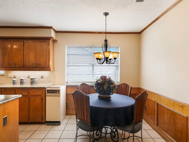 16707 Rugby Ct, Spring, TX 77379 - kitchen featuring a chandelier, brown cabinetry, light tile patterned flooring, a textured ceiling, and a wainscoted wall