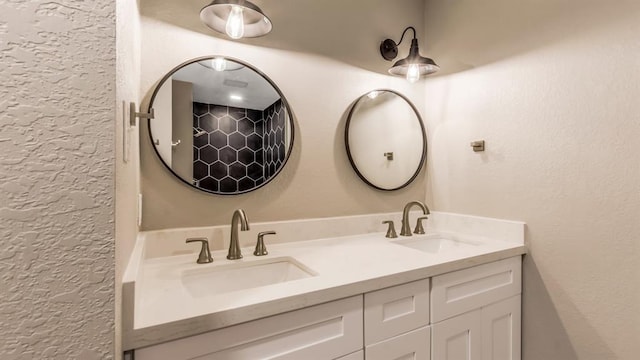 full bath with double vanity, a sink, and a textured wall
