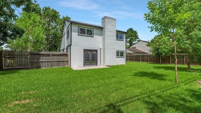 back of property with a chimney, a fenced backyard, stucco siding, a lawn, and french doors